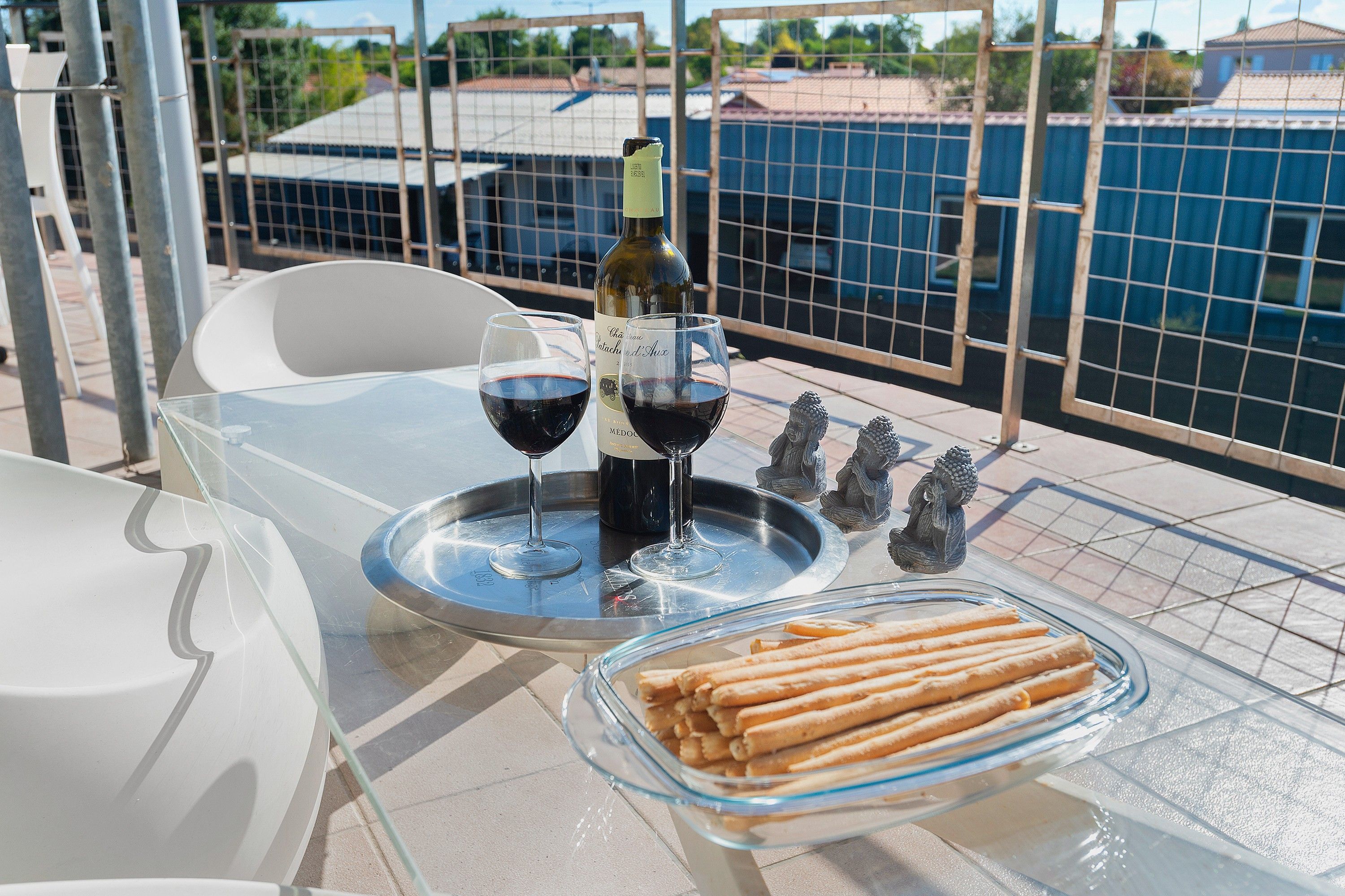 A table with a bottle of wine, two glasses, a tray with crackers, and a Buddha statue.