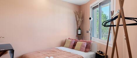 A bedroom with a bed, a window, a desk, and a hanging coat rack.