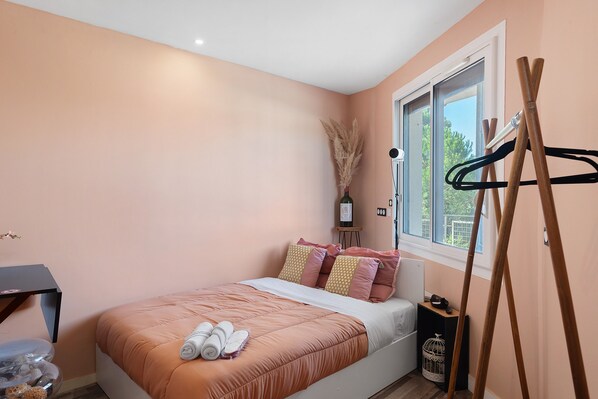 A bedroom with a bed, a window, a desk, and a hanging coat rack.