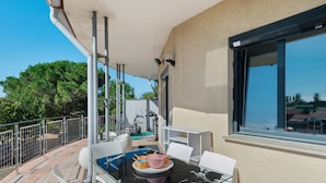 Ein Balkon mit einem Glastisch, weißen Stühlen und Blick auf Bäume und Gebäude.