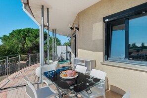 Een balkon met een glazen tafel, witte stoelen en uitzicht op bomen en gebouwen.