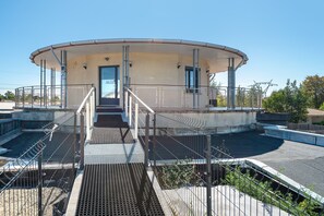 Een rond gebouw met een centrale trap, metalen leuningen en een plat dak.