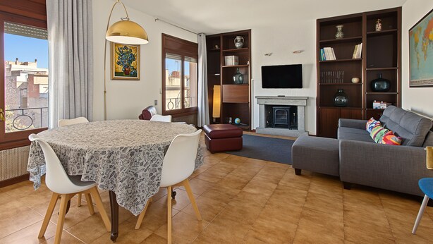 Uma sala de estar com mesa de jantar, sofá, lareira e televisão na parede.