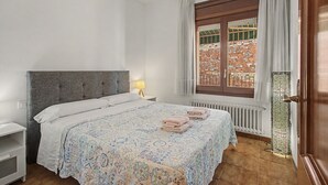 Quarto de hotel com cama, mesa de cabeceira, janela com cortinas e radiador.