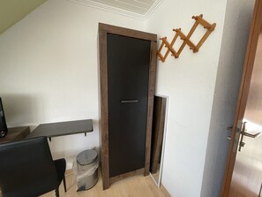 Una habitación con una puerta oscura, una escalera de madera, un pequeño cubo de basura y un escritorio con una silla.