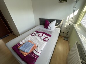 Una cama bien hecha con un edredón estampado, almohadas y toallas dobladas.