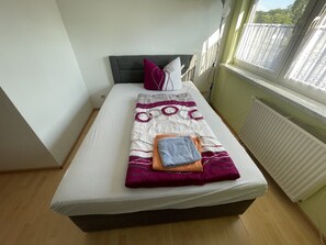 Ein Einzelbett mit grauem Kopfteil, einer weißen Matratze und einer gemusterten Decke.