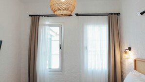 A room with a bed, a window with curtains, a door, and a hanging light fixture. - Pera Locale Alaçatı (Cesme)
