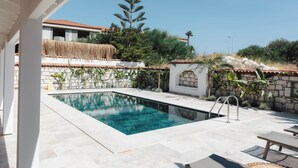 A swimming pool with a stone wall and a thatched roof structure in the background. - Pera Locale Alaçatı (Cesme)