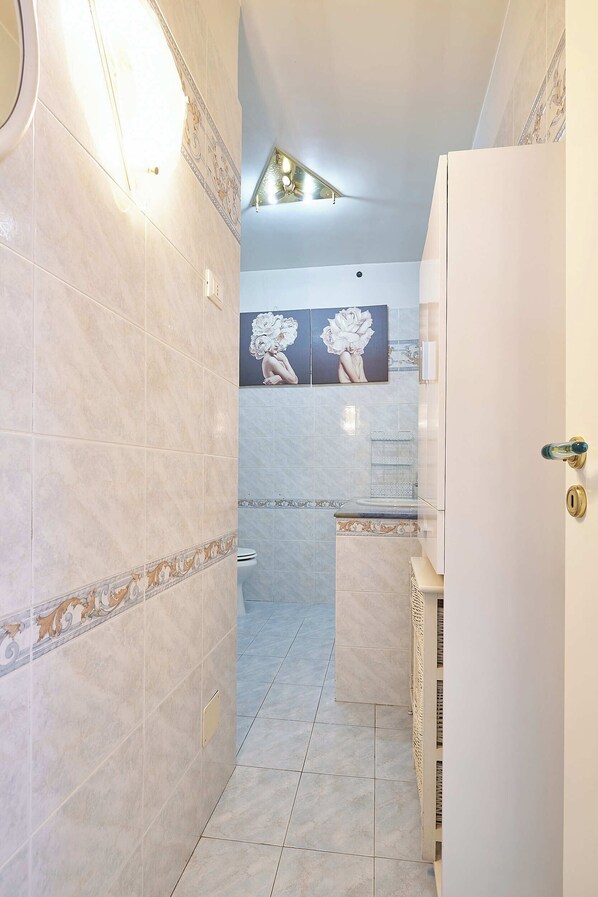 Um banheiro com piso em azulejo, vaso sanitário branco, pia com painel de azulejos decorativos e área de chuveiro.
