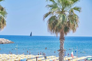 Ein Strand mit Sonnenschirmen, Palmen und einem Segelboot in der Ferne.