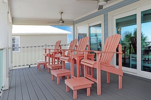 A covered outdoor deck with wooden chairs and tables, a ceiling fan, and a view of a house and palm trees. - Private Pool | Beachfront Decks | Walk to Beach | Cottage By The Sea (St. Joe Beach)