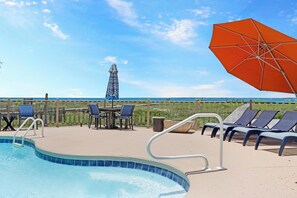 A poolside area with lounge chairs, a table, and an umbrella. - Private Pool | Beachfront Decks | Walk to Beach | Cottage By The Sea (St. Joe Beach)