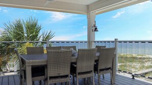 Ein überdachter Außenbereich mit Tisch und Stühlen, einem Deckenventilator und Blick auf den Strand.