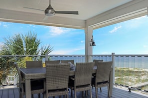 Ein überdachter Außenbereich mit Tisch und Stühlen, einem Deckenventilator und Blick auf den Strand.
