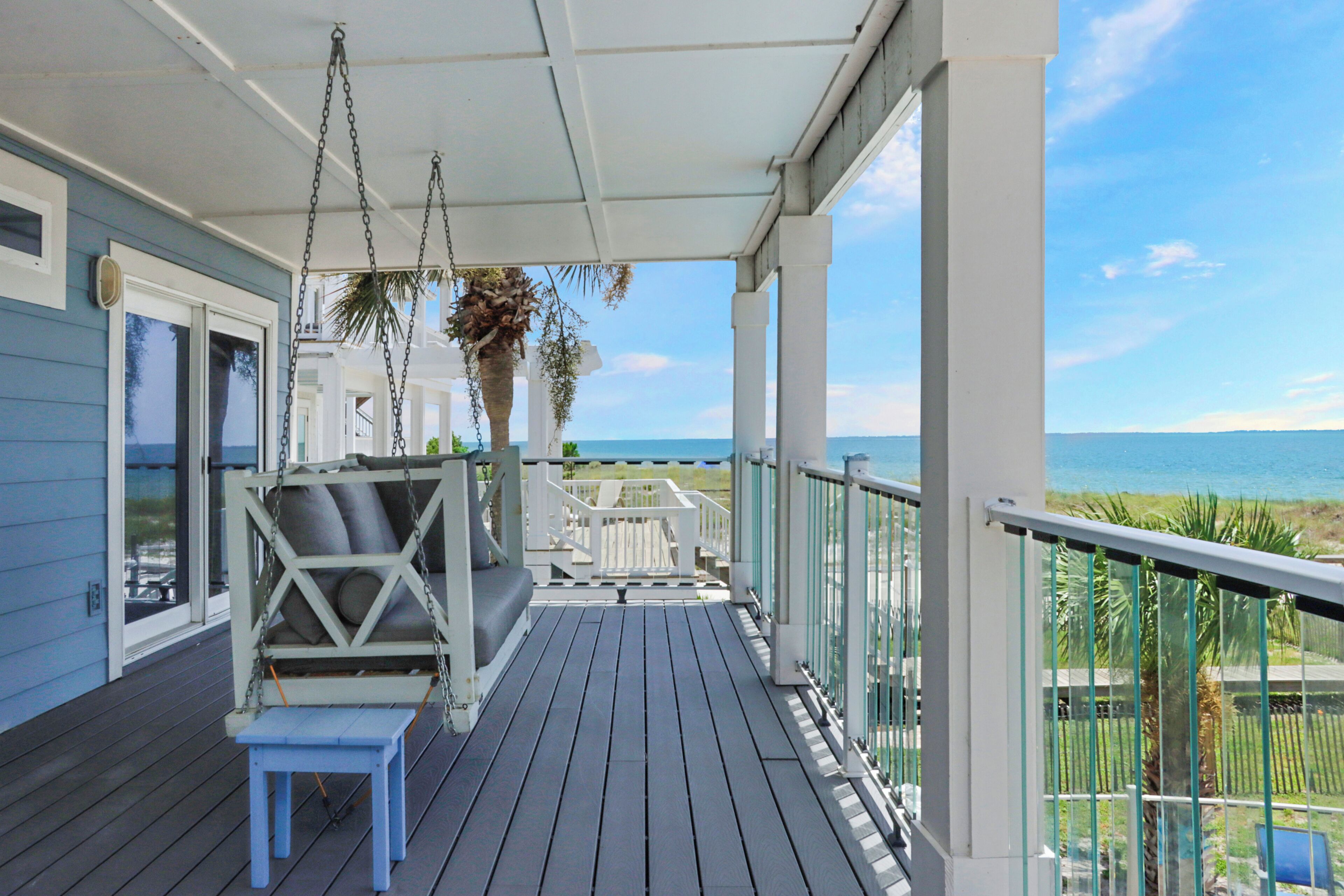 A covered porch with a swing chair, a small table, and a view of the ocean.