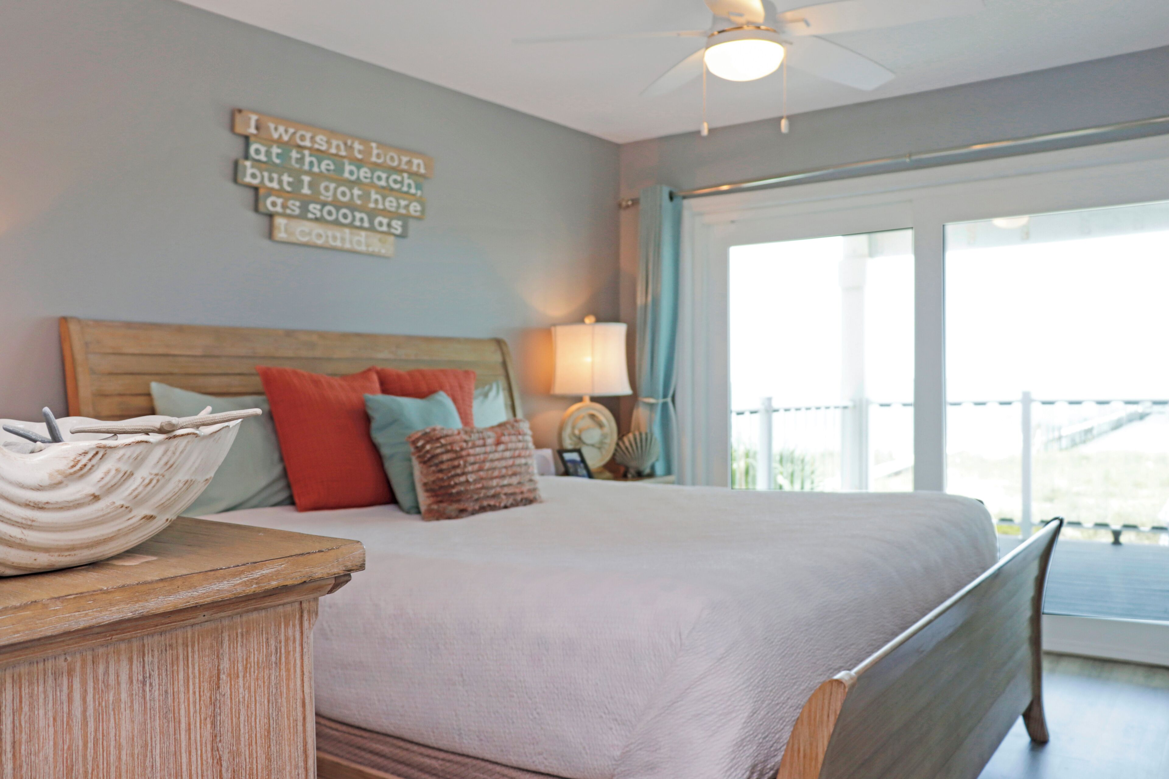 A bedroom with a bed, pillows, a bedside table, a lamp, and a wall with a motivational quote.
