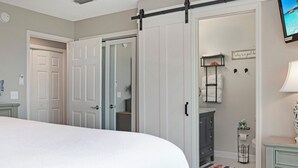 Ein Schlafzimmer mit einem Bett, einem Schiebetürenschrank, einem Schminktisch mit Spiegel und einem an der Wand montierten Fernseher.