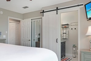 Ein Schlafzimmer mit einem Bett, einem Schiebetürenschrank, einem Schminktisch mit Spiegel und einem an der Wand montierten Fernseher.