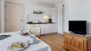 Une cuisine compacte avec des meubles blancs, une machine à café et un téléviseur posé sur un meuble en bois.