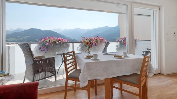 Un balcon avec une table dressée pour deux personnes, offrant une vue sur un paysage montagneux.