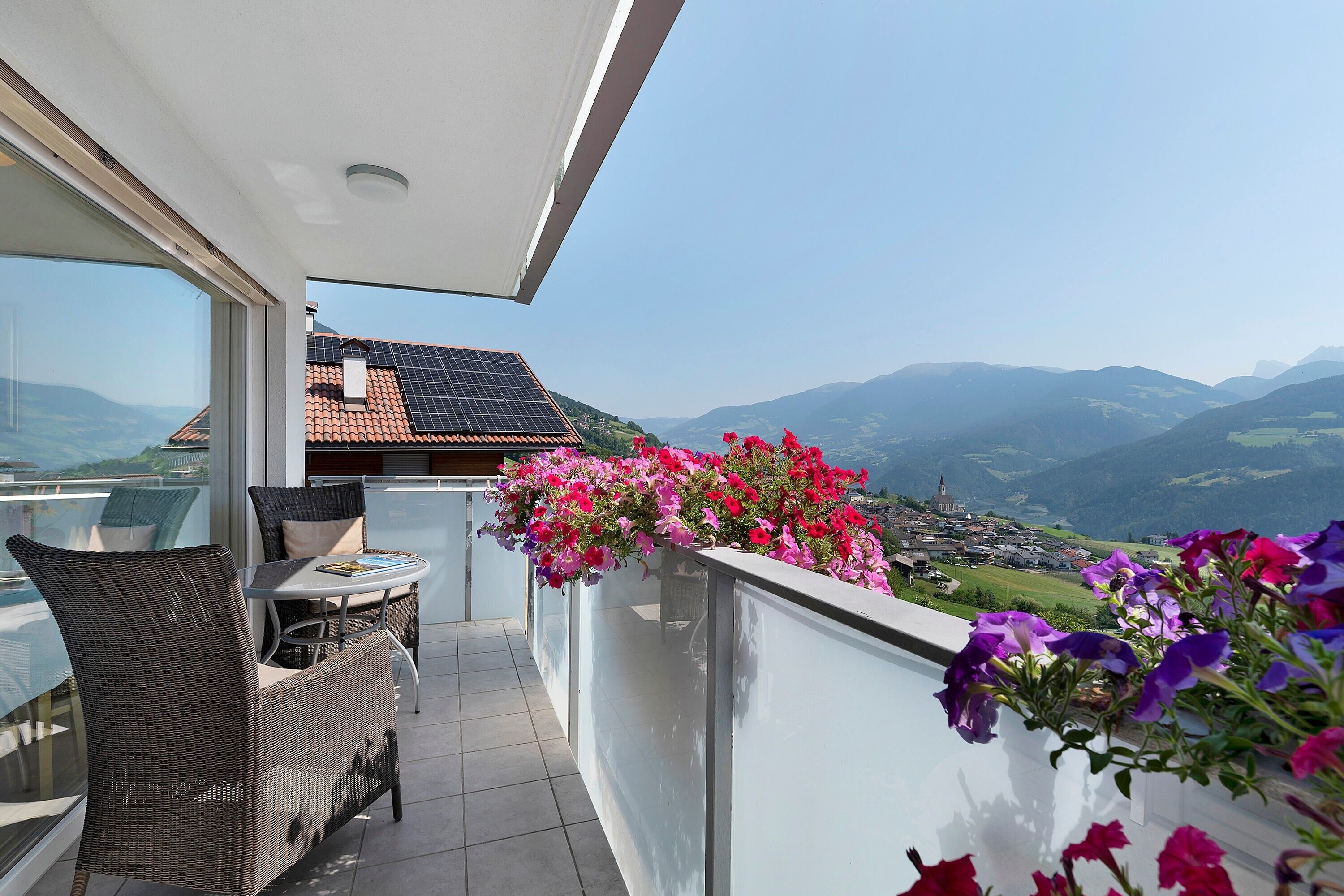Un balcon avec un fauteuil en osier, une petite table et un arrangement floral.