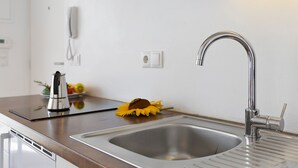 Une cuisine moderne avec un évier en acier inoxydable, une hotte intégrée et une seule fleur posée sur le plan de travail.