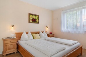 A bedroom with a wooden bed, white bedding, two bedside tables with lamps, a wall-mounted painting, and a window with sheer curtains. - Apartment 'Wiesenrain  Bergblick' with Mountain View, Shared Garden and Wi-Fi (Feldthurns)