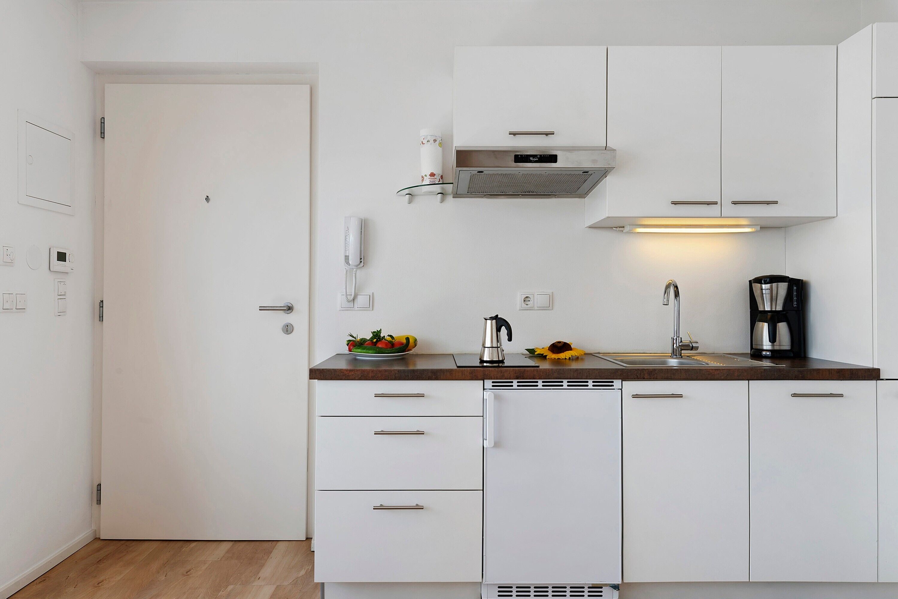 A compact kitchen with white cabinetry, a coffee maker, and a fruit bowl.