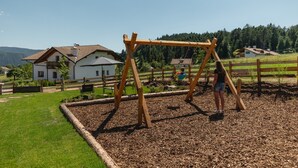 A playground with a wooden swing set and a child swinging. - Holiday Apartment 'Am Oberranhof' with Mountain View, Shared Terrace, and Wi-Fi (Deutschnofen)