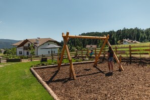 Ein Spielplatz mit einer Holzschaukel und einem Kind, das schaukelt.