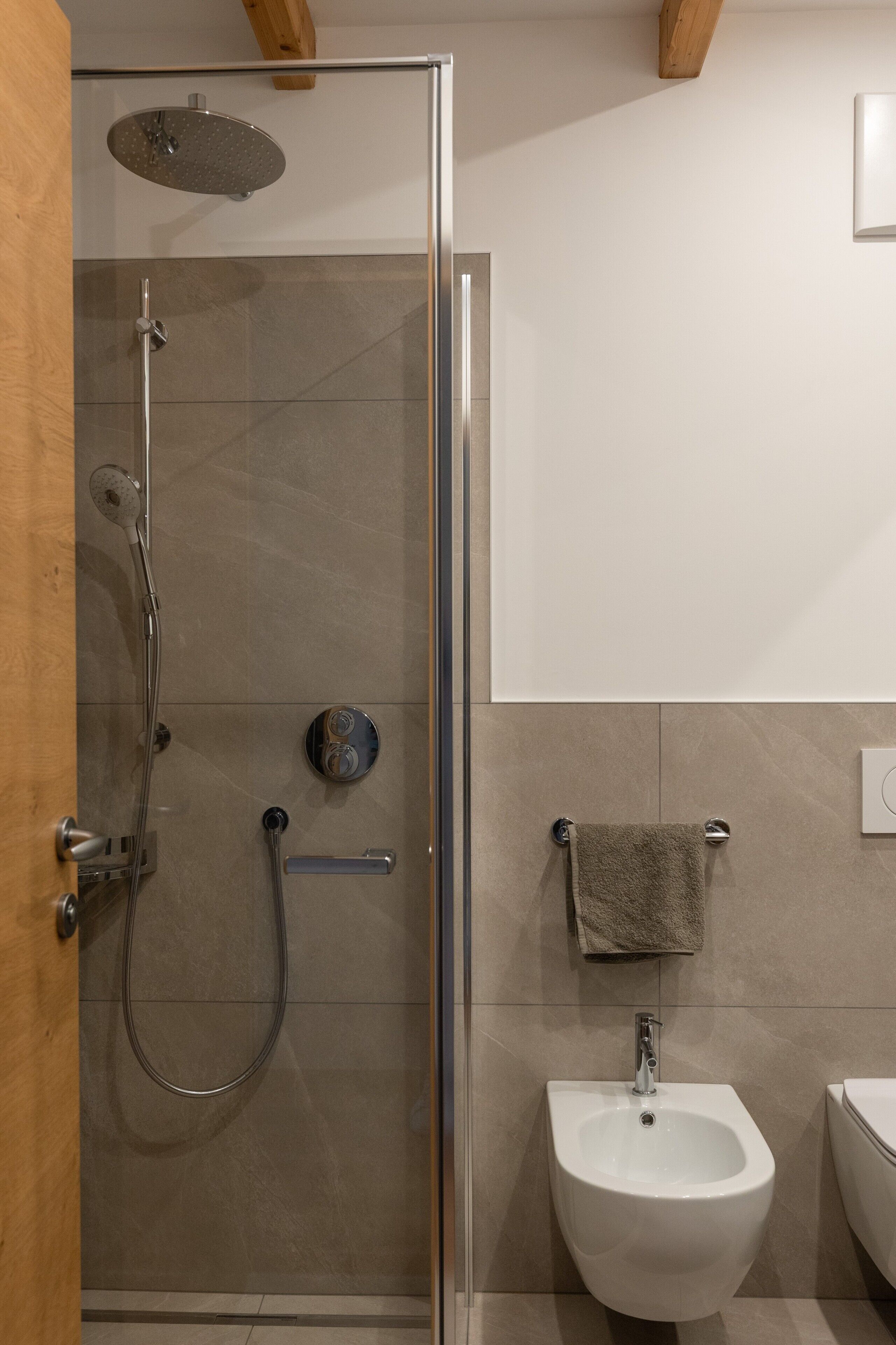 A modern bathroom with a glass-enclosed shower, a white pedestal sink, and a towel rack.