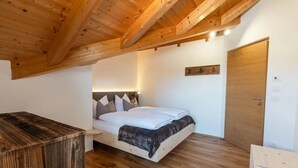 A bedroom with a wooden ceiling, a bed with white bedding, a bedside table, and a door. - Holiday Apartment 'Am Oberranhof' with Mountain View, Shared Terrace, and Wi-Fi (Deutschnofen)