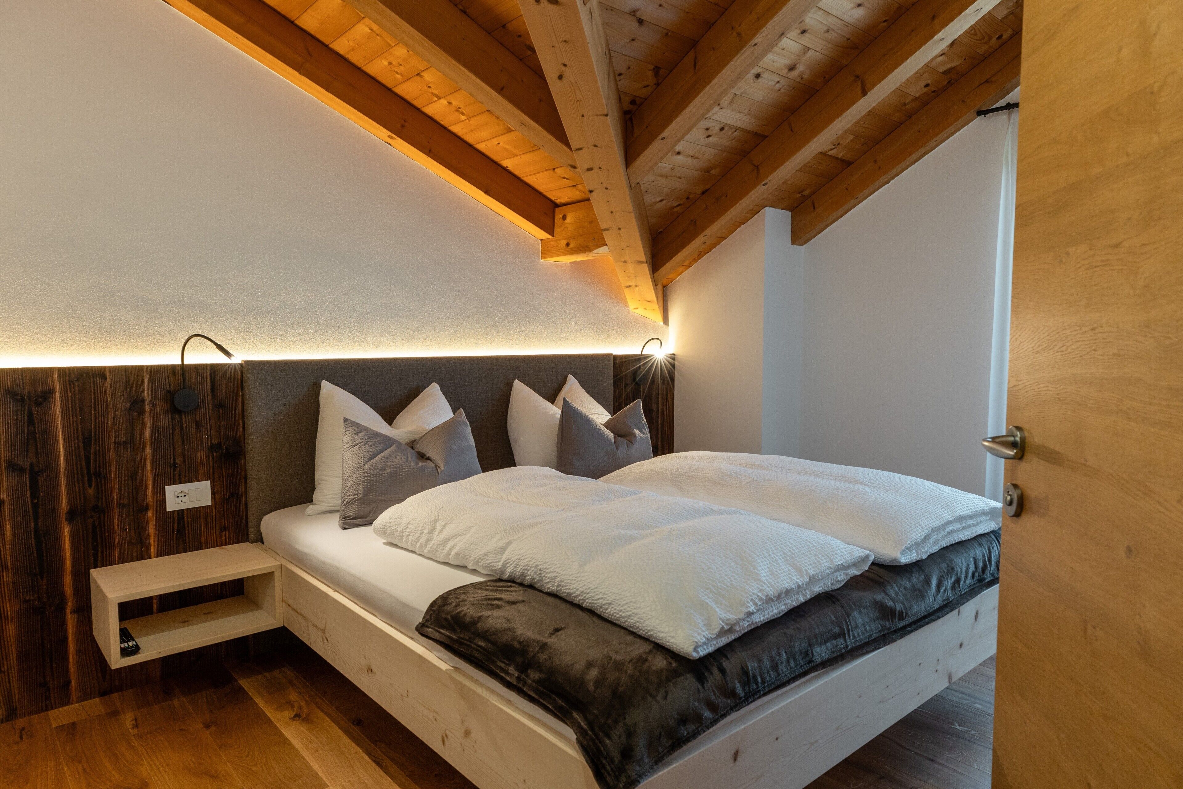 Ein Schlafzimmer mit Holzbalkendecke, einem Bett mit vielen Kissen, einem Nachttisch und einem Beistelltisch.