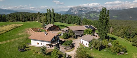 A rural property with multiple buildings, including a main house and barns, surrounded by lush greenery and mountains in the background.