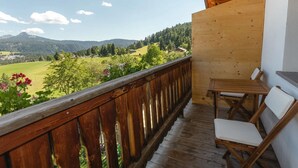 A wooden balcony with a table and chairs, overlooking a green landscape with mountains. - Holiday Apartment 'Am Oberranhof' with Mountain View, Shared Terrace, and Wi-Fi (Deutschnofen)