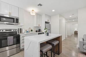 A modern kitchen with white cabinetry, stainless steel appliances, and a marble island with bar stools.