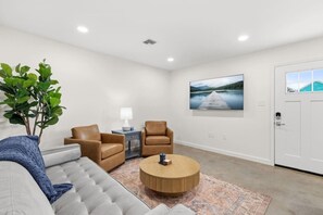 A modern living room with a sofa, two armchairs, a coffee table, a lamp, a plant, and a large landscape painting on the wall. - 6 Bedrooms Perfect for Large Groups (Lafayette)
