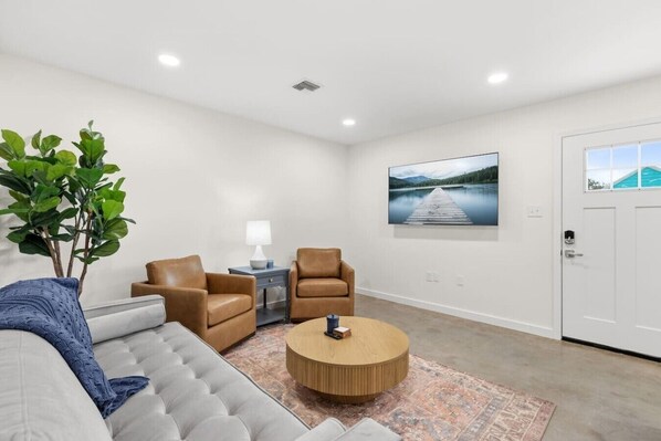 A modern living room with a sofa, two armchairs, a coffee table, a lamp, a plant, and a large landscape painting on the wall.
