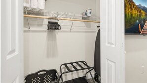 Um quarto com uma porta branca, uma cadeira preta e branca, uma estante com objetos e uma pintura de um lago.