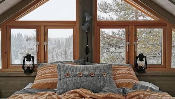Una habitación acogedora con techo inclinado, ventanas amplias y una cama con ropa de cama estampada.