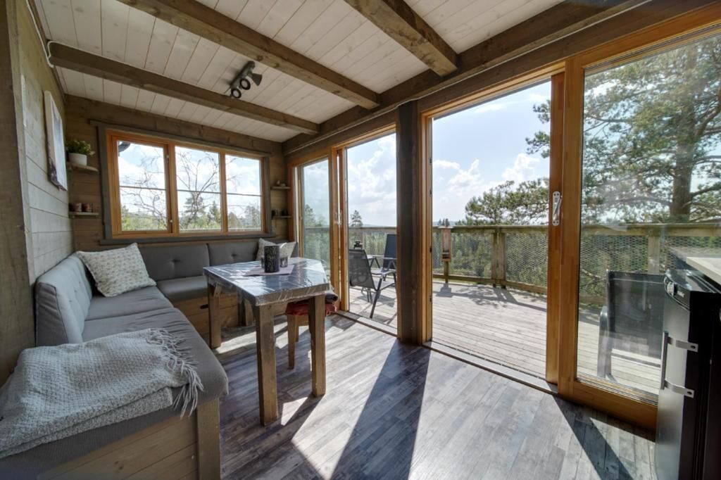 A cozy cabin interior with a wooden ceiling, a sofa, a table, and a large sliding glass door leading to an outdoor deck.