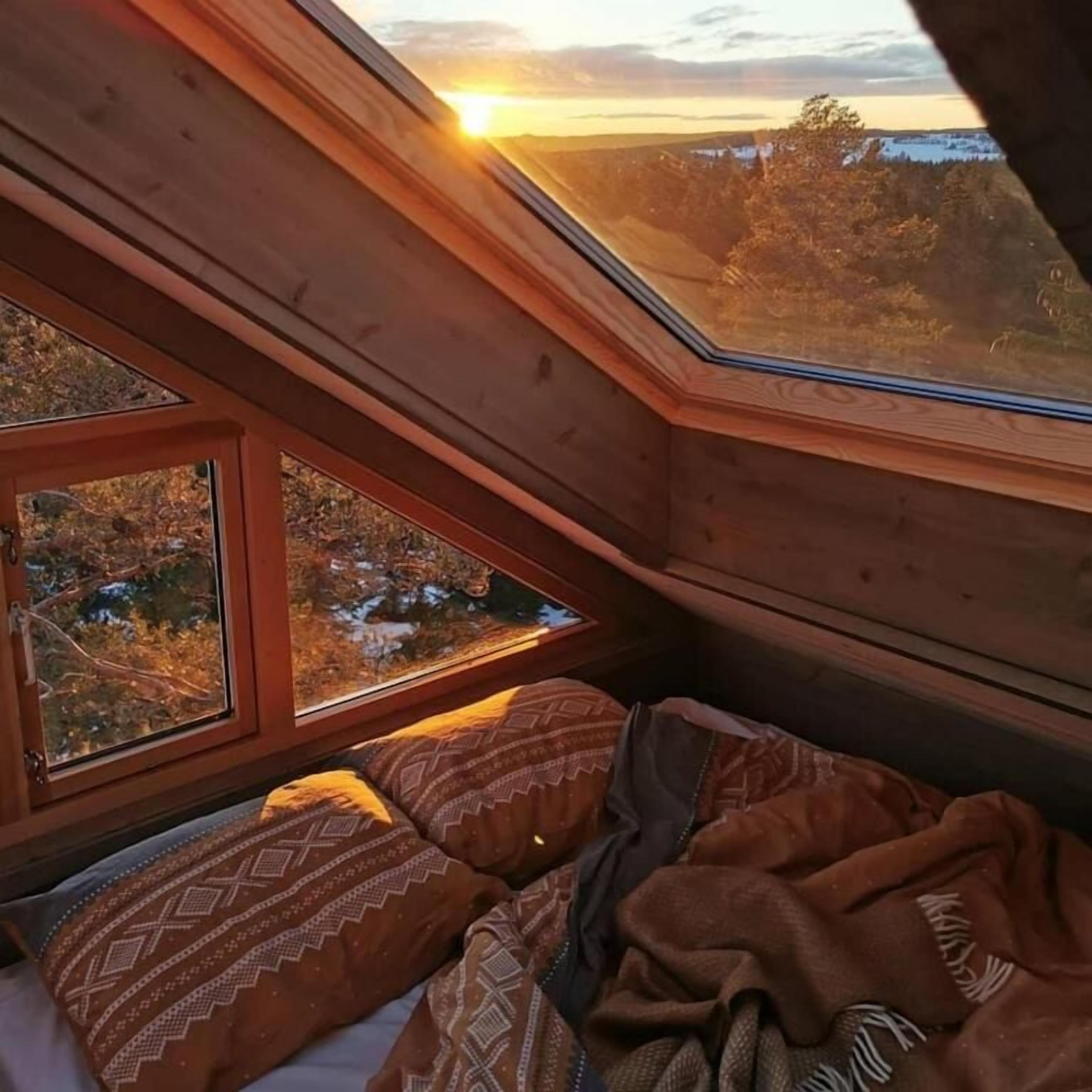 Une chambre à coucher avec un plafond en pente et une grande fenêtre donnant sur un paysage enneigé.