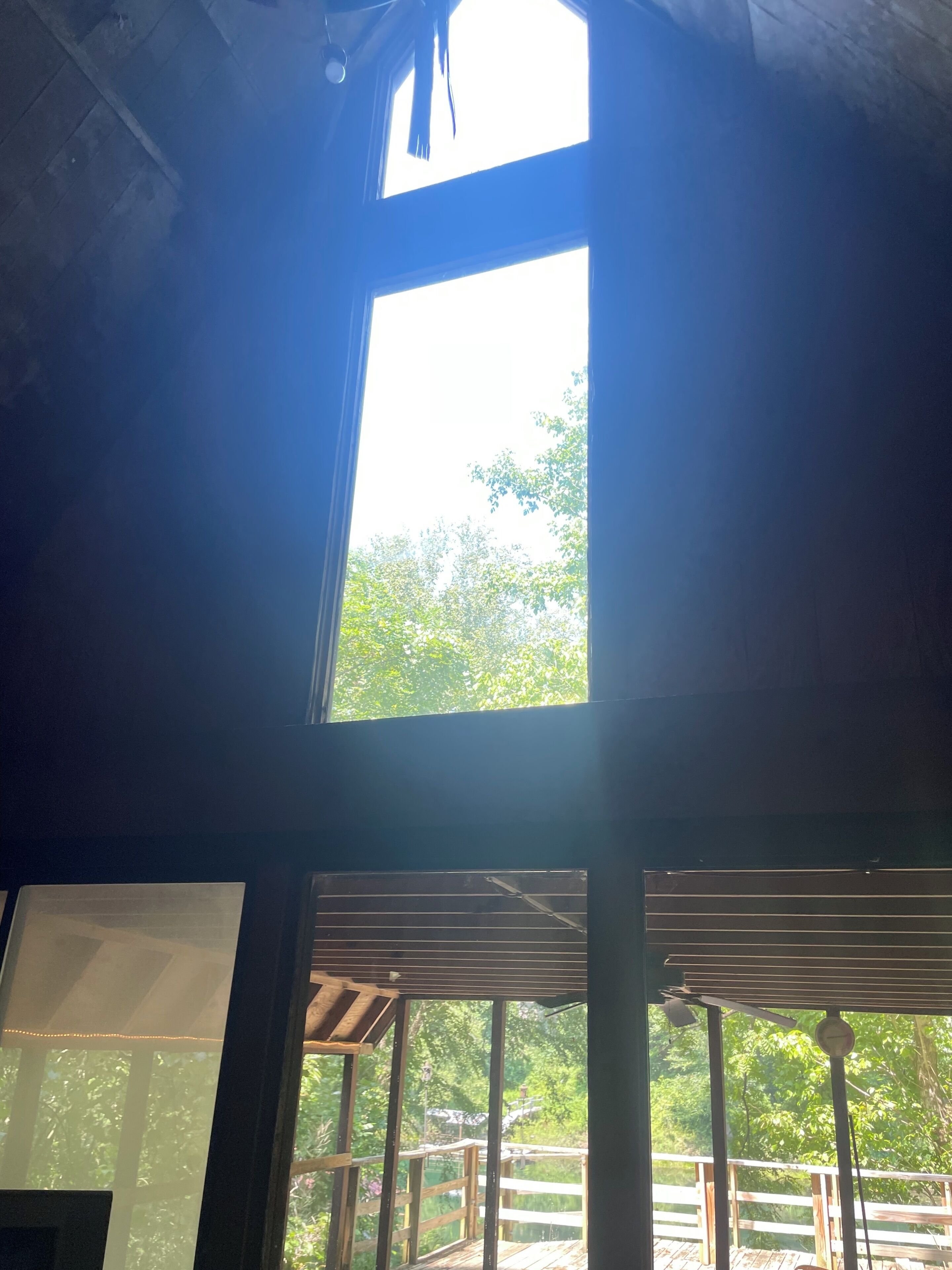 A room with a large window, wooden beams, and a view of greenery outside.