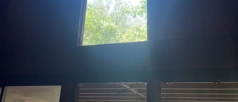 A room with a large window, wooden beams, and a view of greenery outside.