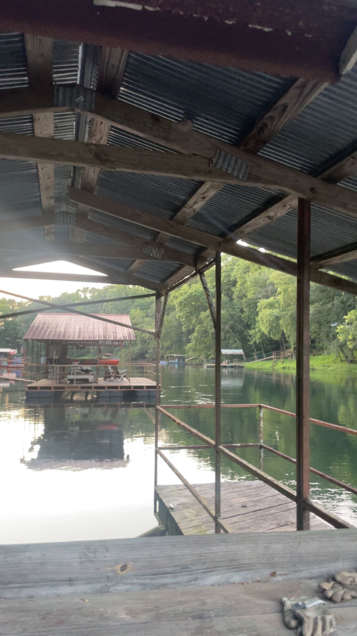 A covered dock with a view of a lake and a small building in the background.