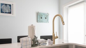 Una cocina con un lavamanos de acero inoxidable, un grifo dorado y una encimera blanca.