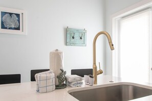 Eine Küche mit einer Spüle aus Edelstahl, einem Wasserhahn in Goldfarbe und einer weißen Arbeitsplatte.