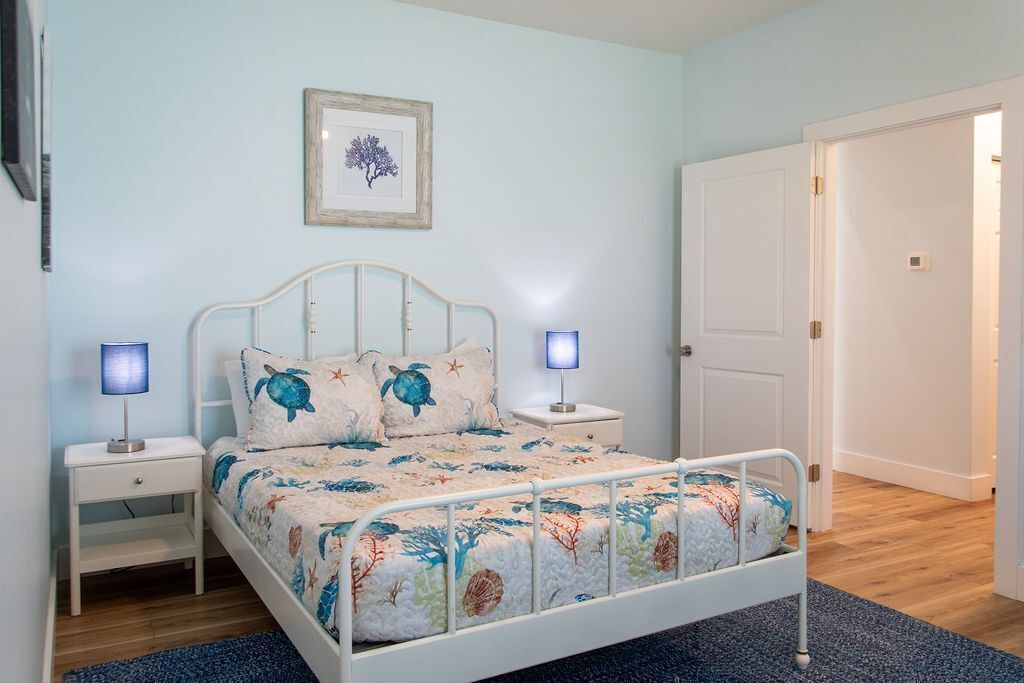 Ein Schlafzimmer mit einem Bett, Nachttischen, einem gerahmten Bild an der Wand und einer Tür.