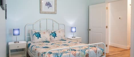 A bedroom with a bed, bedside tables, a framed picture on the wall, and a door.